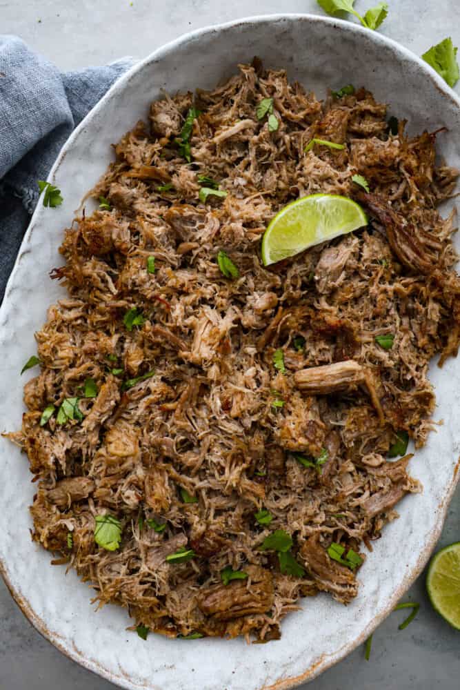 Top-down view of carnitas in a large serving dish, garnished with a lime slice.