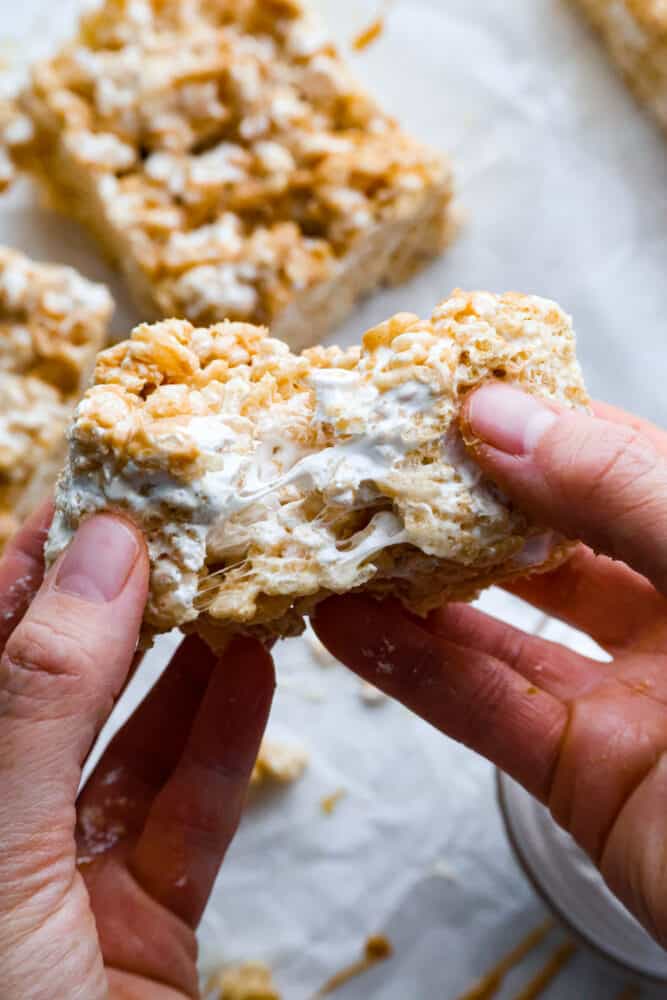 A rice krispie treat being broken in half to reveal the soft, marshmallow-filled inside.