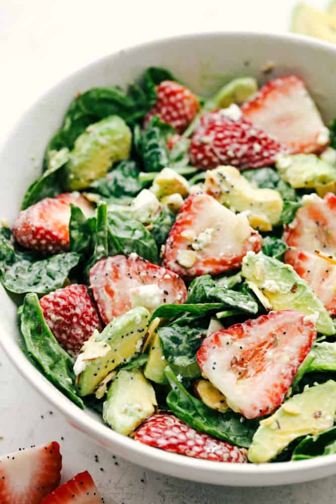 Strawberry avocado spinach salad tossed together in a white bowl and ready to serve. 