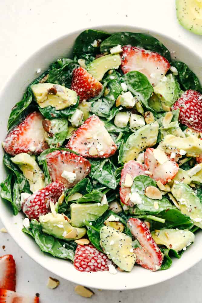 Strawberry, avocado spinach salad with poppyseed dressing mixed together in a white bowl. 