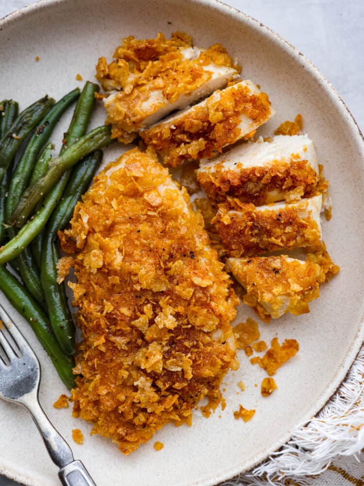 Cornflake chicken and green beans served on a white plate.