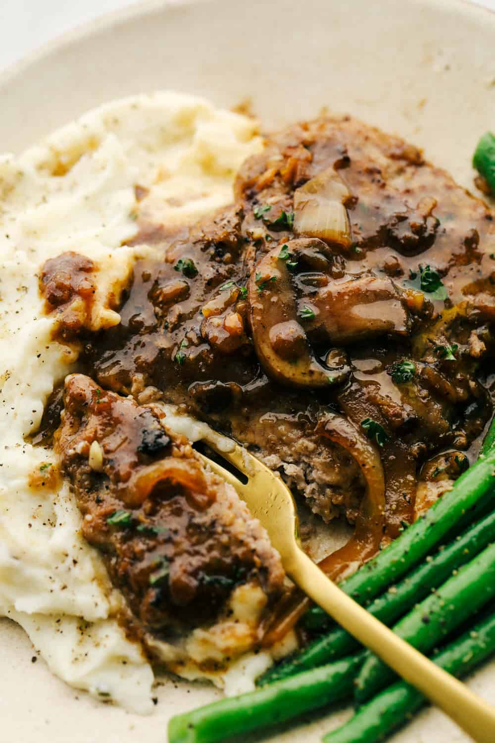 Cube steak with mashed potatoes and mushroom gravy with a side of green beans.
