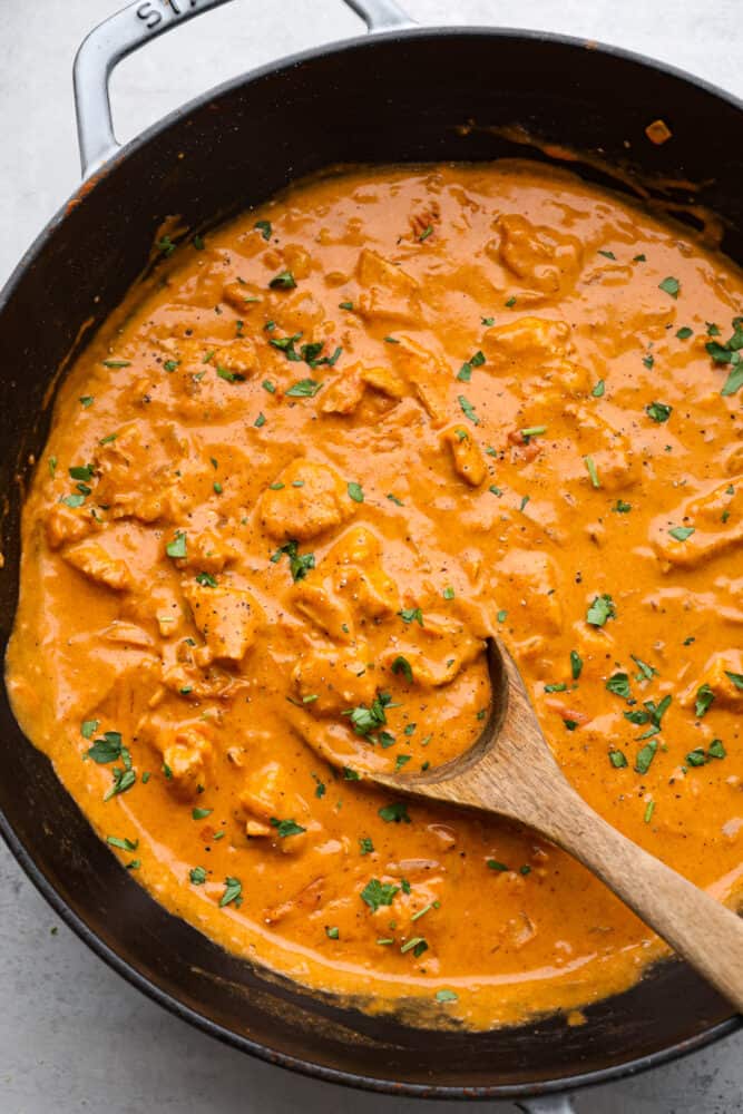 Indulge in a rich and creamy Chicken Paprikash that is so delicious, and it pairs perfectly over noodles. This classic Hungarian dish combines tender chicken with a flavorful blend of smoked paprika, onions, garlic, and tomatoes. The top view of chicken paprikash in a pan with a wooden spoon.
