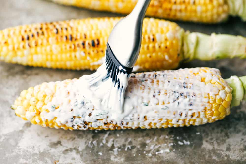 Grilled corn being brushed with mayonnaise.