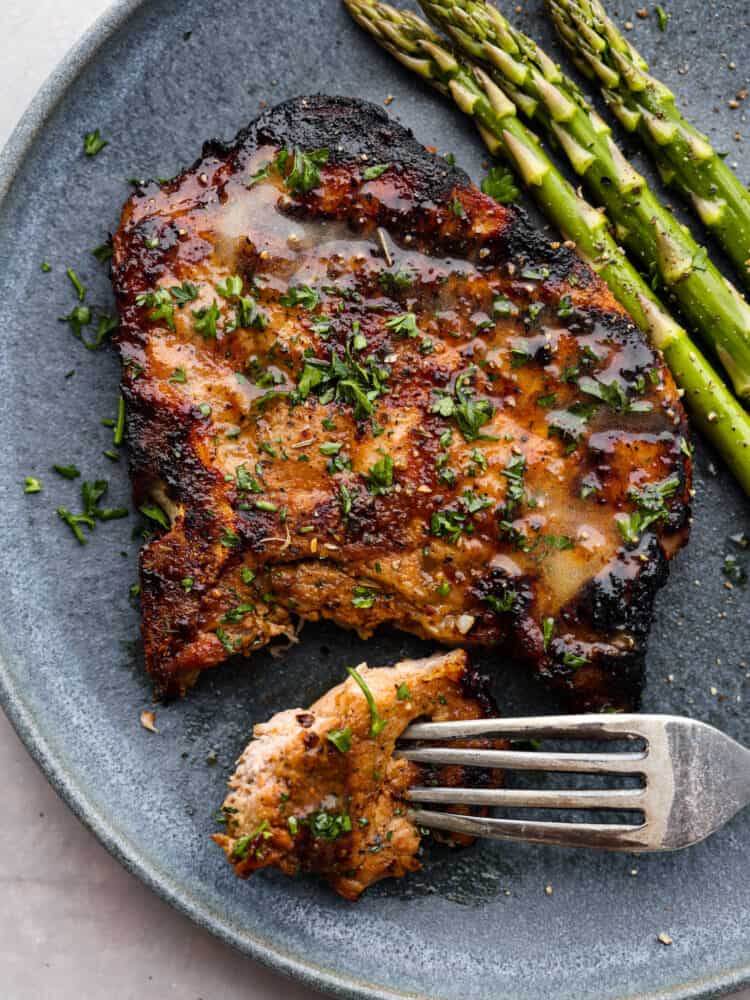 A pork chop served with asparagus. There is a bite taken out of it.