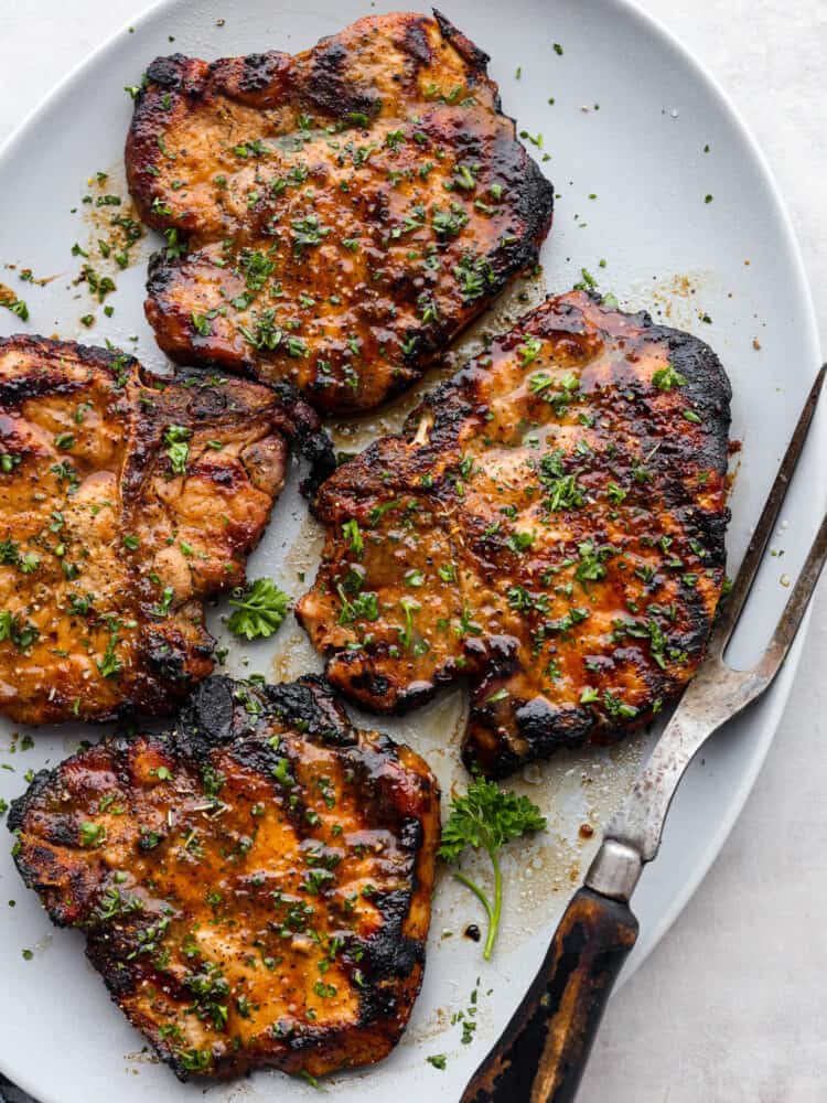 4 grilled pork chops on a white plate.
