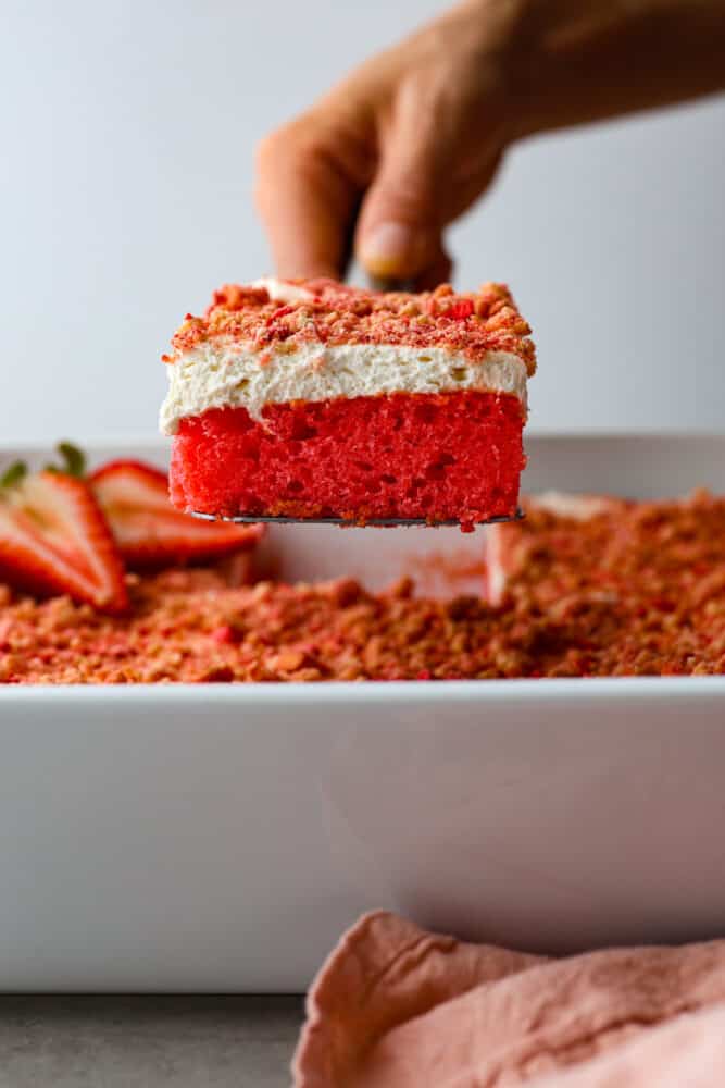 The side view of a piece of strawberry crunch cake being taken out of the pan with a cake server. 