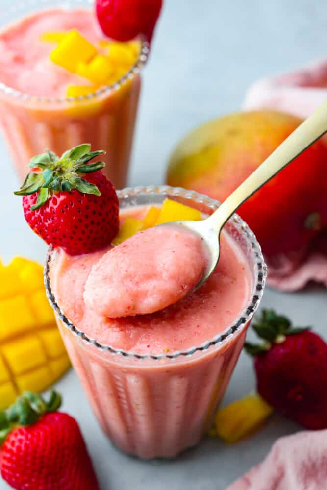 A close up of a spoon in a glass filled with strawberry mango smoothie. 