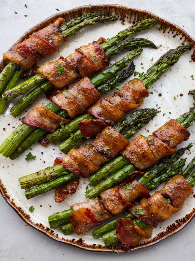 Top-down view of bacon wrapped asparagus on a white and brown plate.
