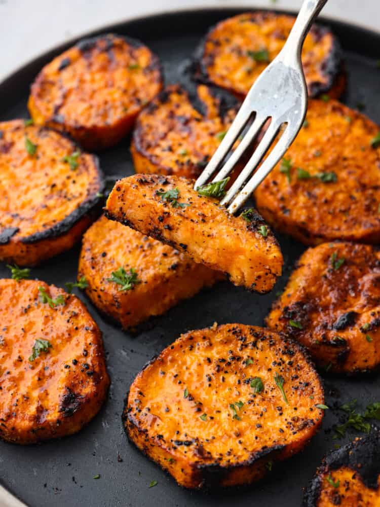 Bursting with flavor and ready in 15 minutes, these grilled sweet potatoes are a must-add to any summer barbecue lineup. Even though they're cooked to smoky perfection, each slice is nice and tender and coated in a tasty blend of savory seasonings. Picking up a piece with a fork.