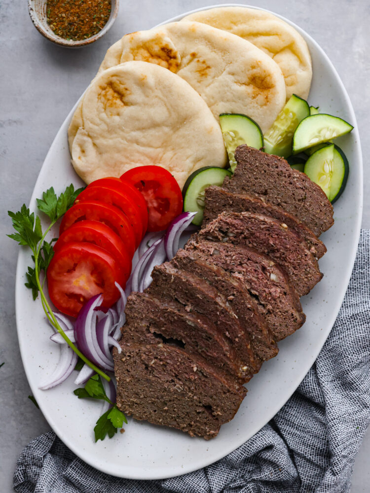 Sliced gyro meat served with tomatoes, onions, cucumber, and pita bread.