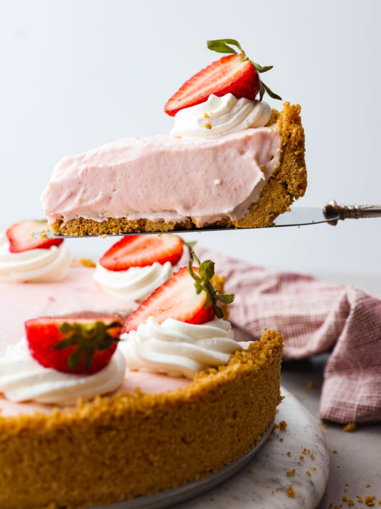 Side view of no-bake strawberry cheesecake with a slice being lifting up with a pie spatula. 