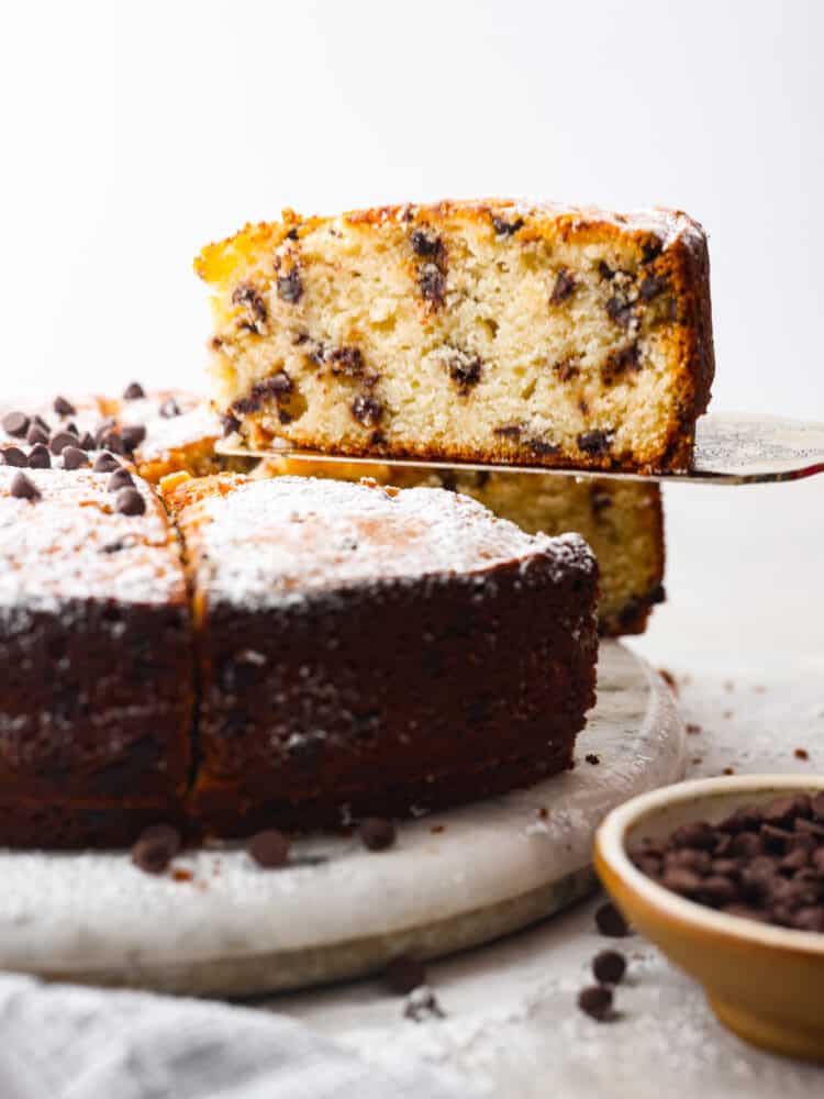 Get ready to indulge in a mouthwatering ricotta cake that will blow your taste buds away! This amazing dessert combines the creamy goodness of whole milk ricotta cheese with pockets of mini chocolate chips. The result is cake that's moist, tender, and perfectly sweet! A slice of chocolate chip ricotta cake being served with a metal spatula.