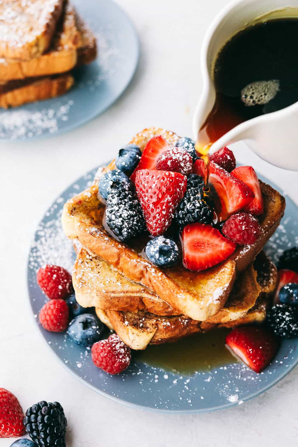 French toast covered with berries, sprinkled with powdered sugar and syrup. 