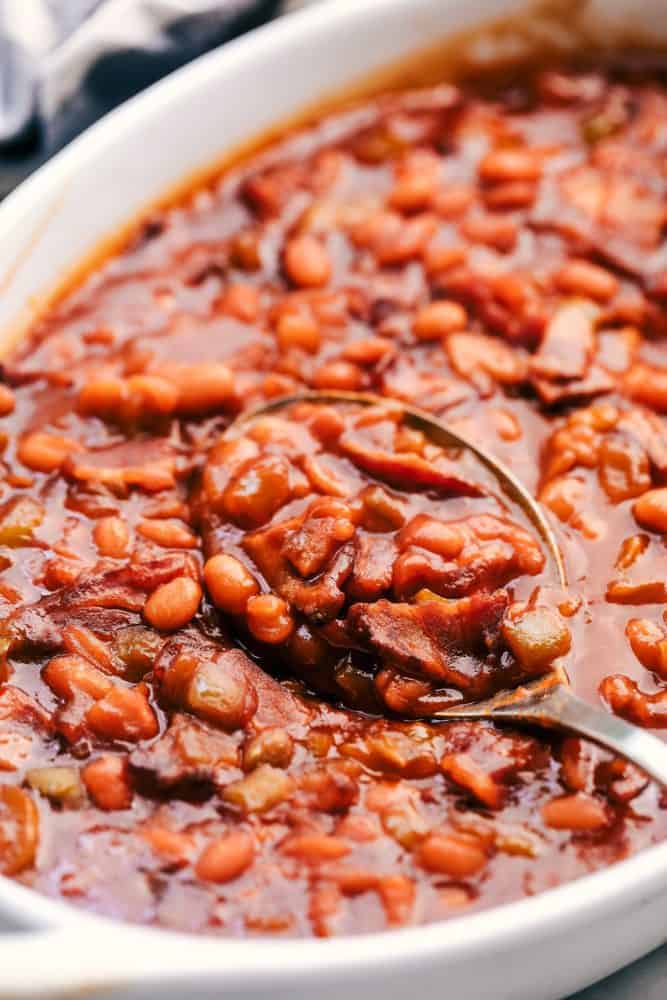 Baked beans in a white platter with a metal spoon. 