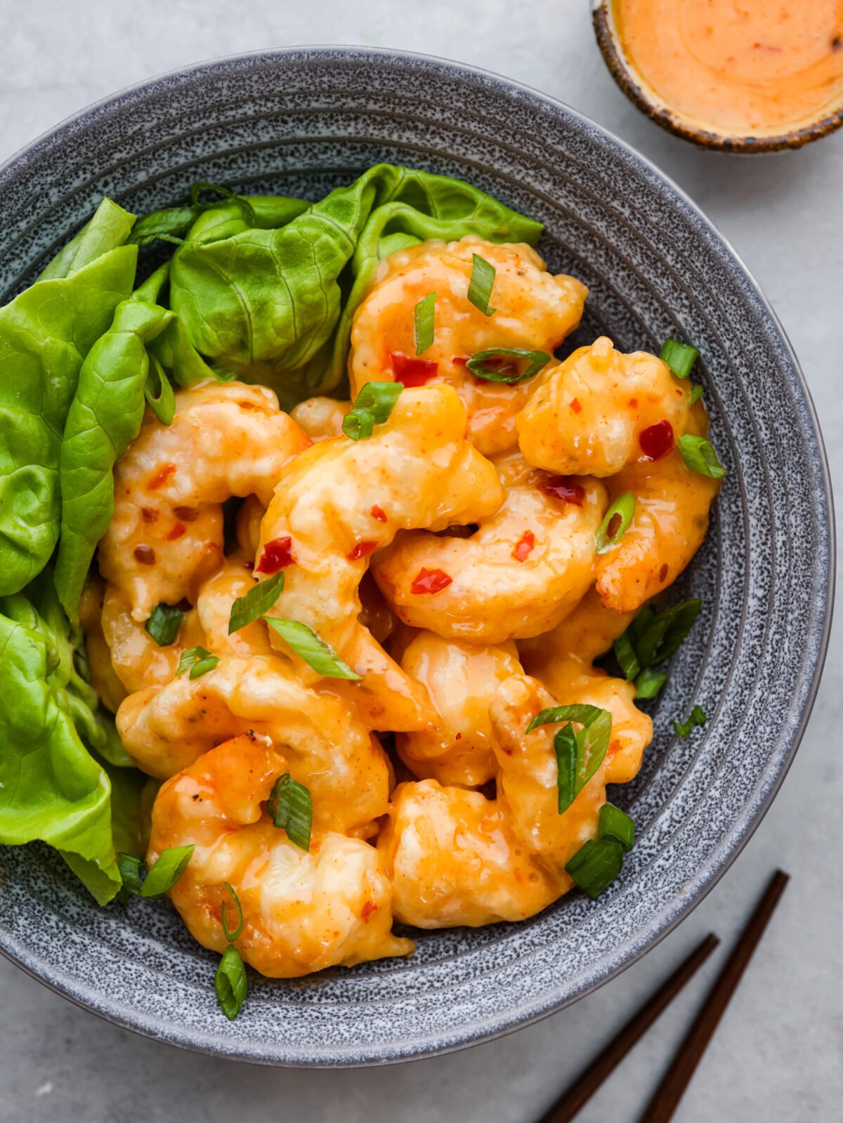 Top-down view of dynamite shrimp served in a stoneware bowl with greens.
