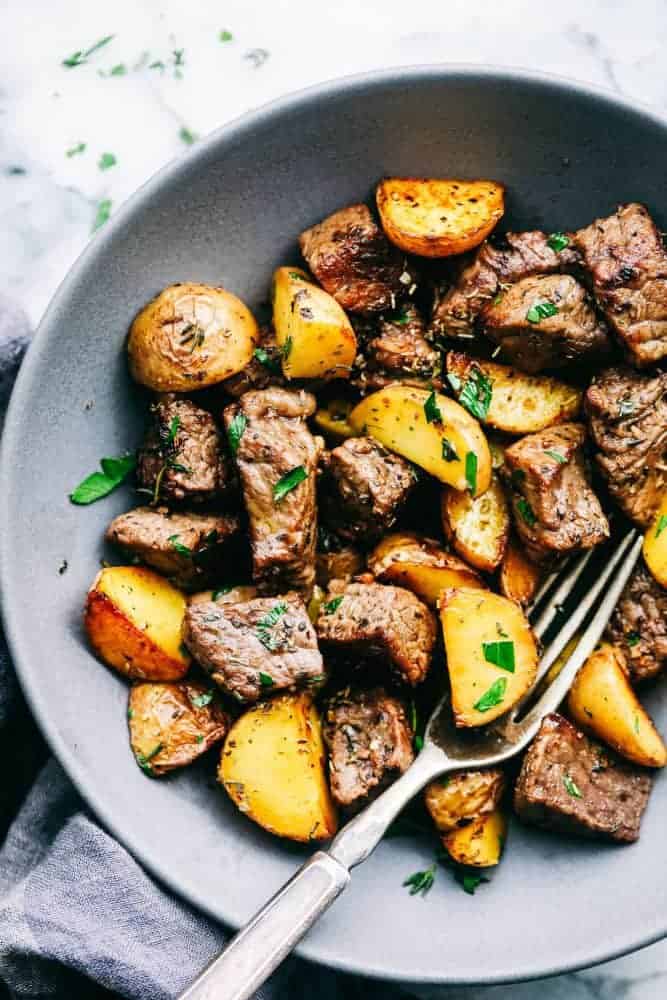 Garlic Butter Herb Steak Bites with Potatoes in a grey bowl with a metal spoon. 
