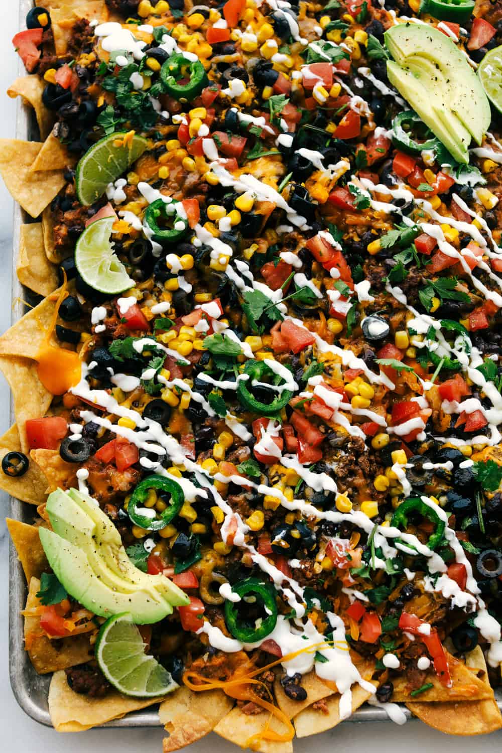 Oven baked sheet pan nachos with sour cream and avocado over top.