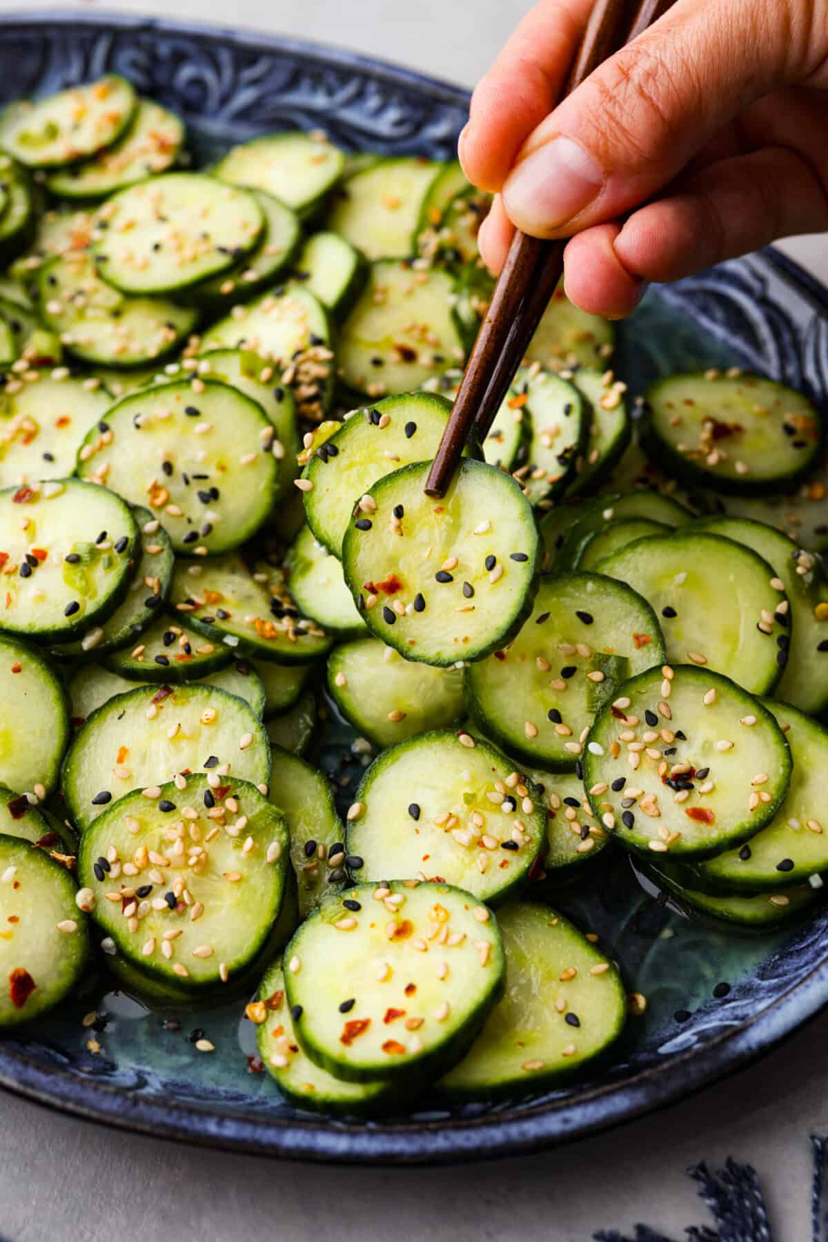 A pair of chopsticks lifting a slice of cucumber out of the bowl. 