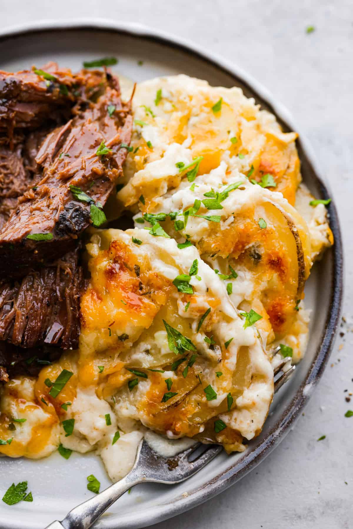 Close top view of au gratin potatoes on a gray plate served with shredded beef on the side.