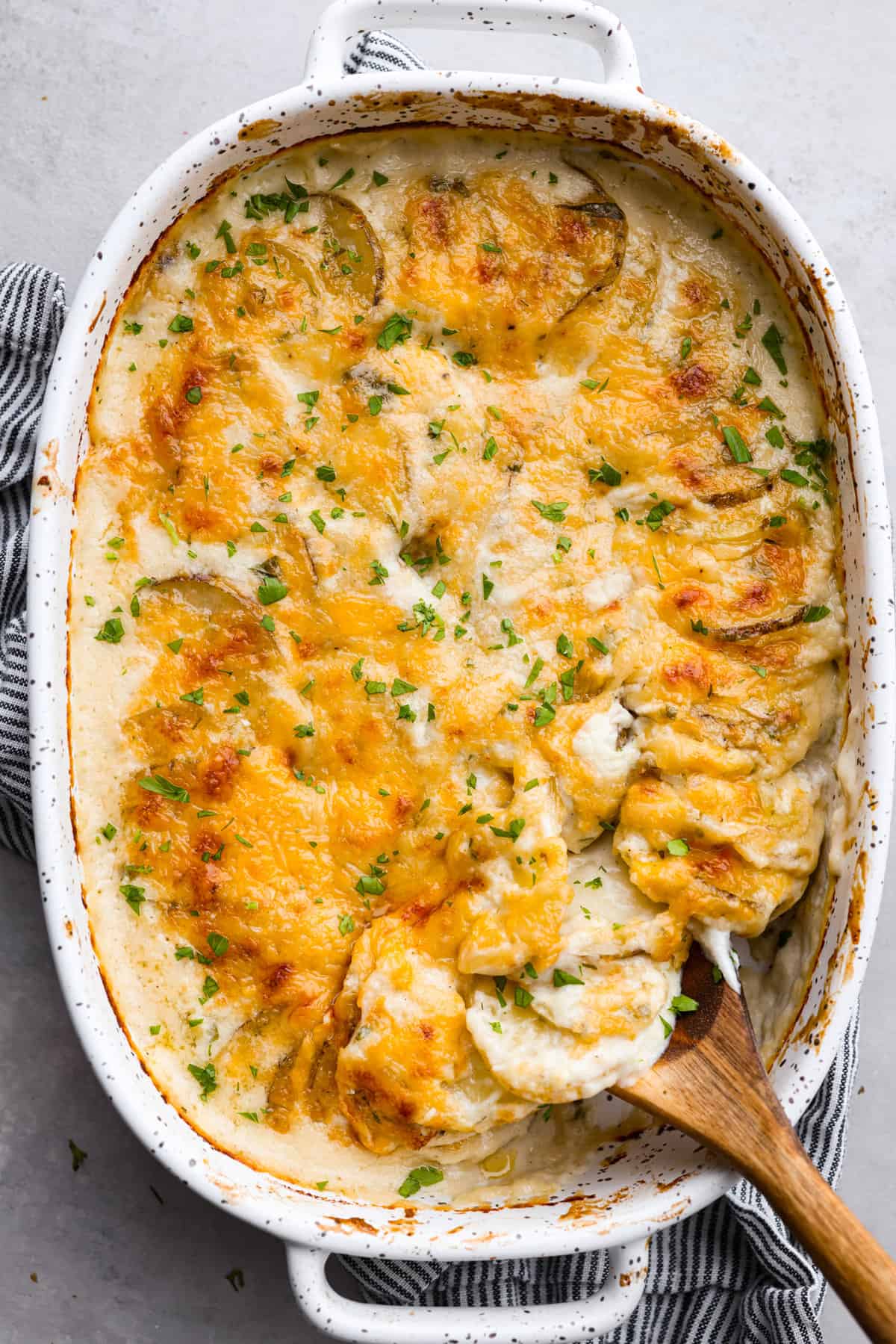 Top view of au gratin potatoes in a white baking dish with a wood serving spoon.