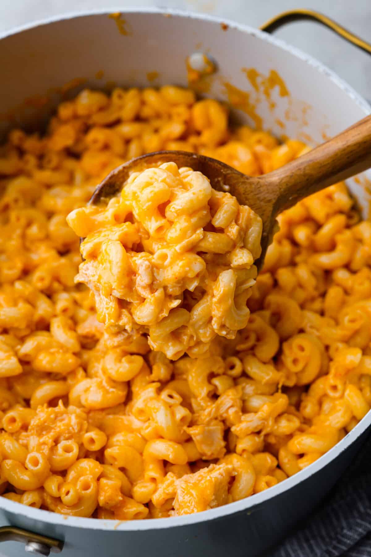 Close view of buffalo chicken mac and cheese cooked in a large pot with a wood spoon lifting up macaroni.