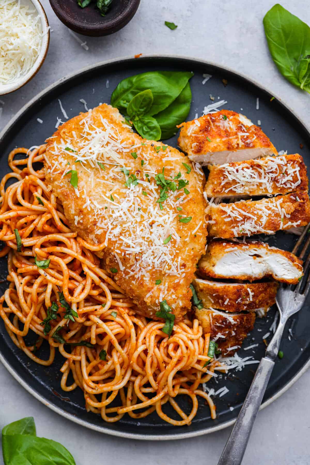 Chicken romano served on a dark blue plate with spaghetti noodles.