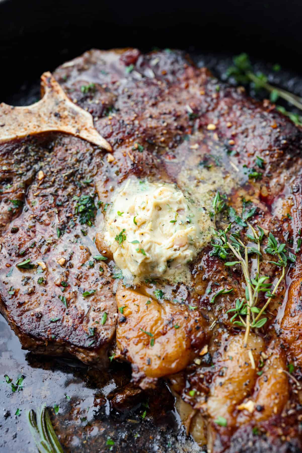 Close view of cowboy butter melting on top of a cooked steak garnished with fresh herbs.