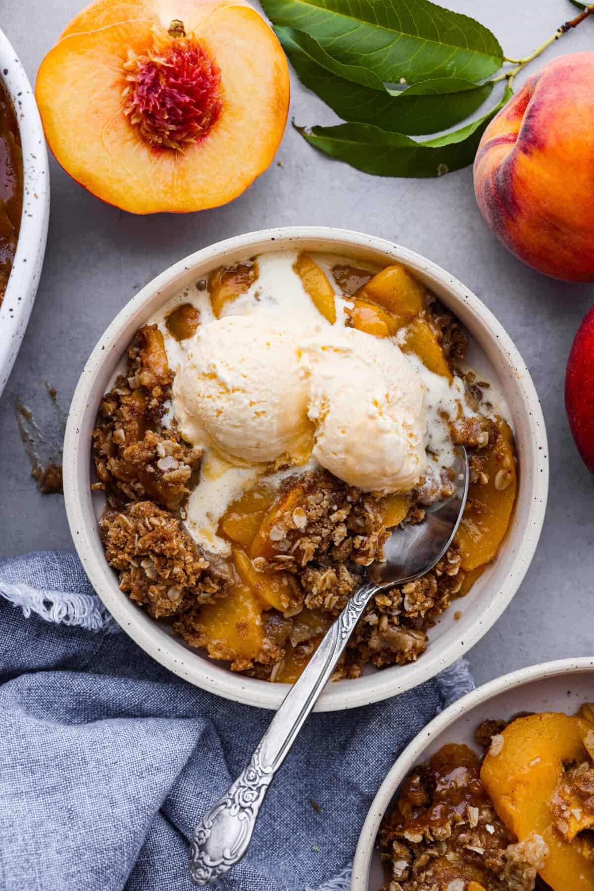 The top view of a bowl of peach crisp with a scoop of vanilla ice cream on top. 