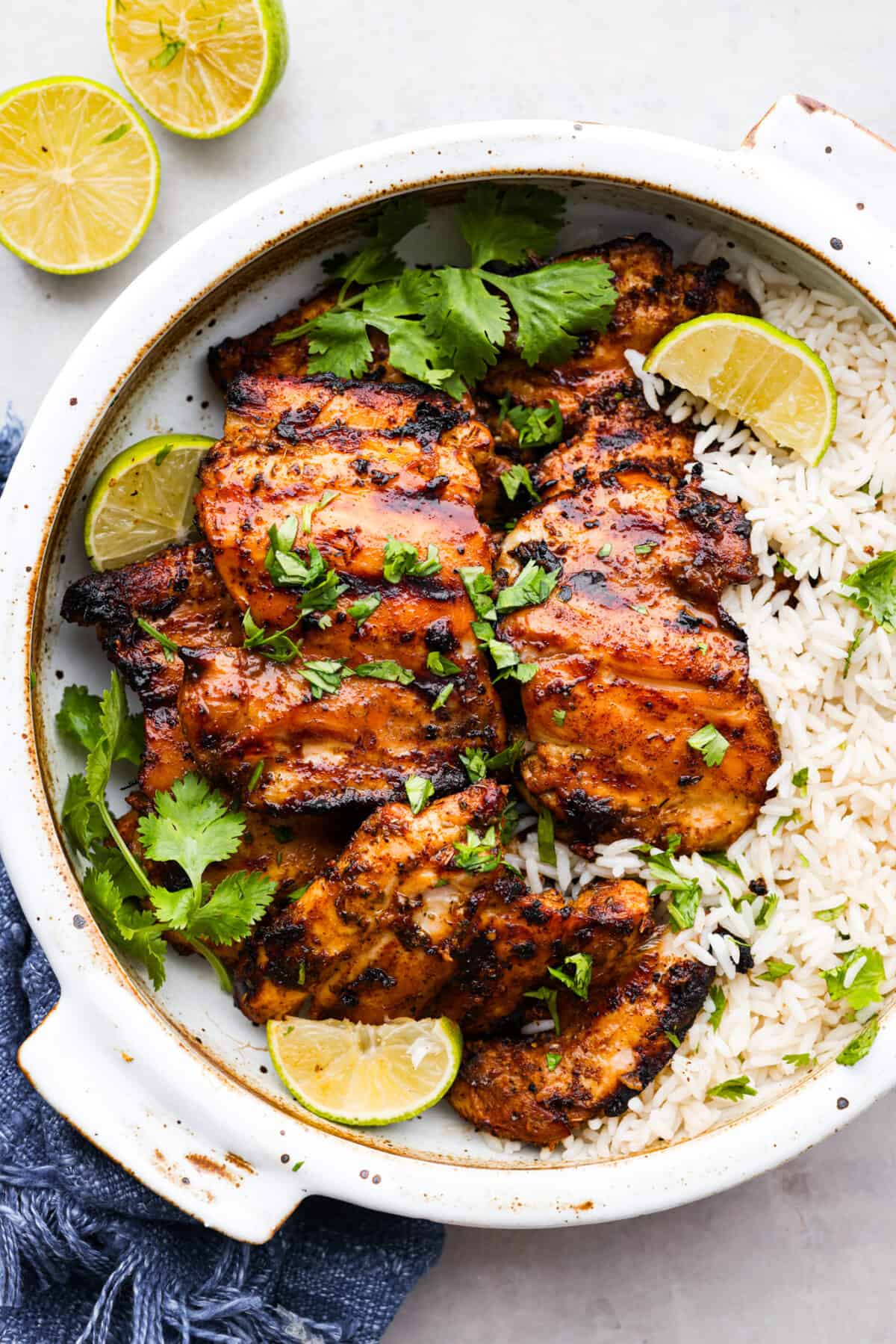 Mexican grilled chicken served over rice. It's garnished with fresh herbs and lime slices.