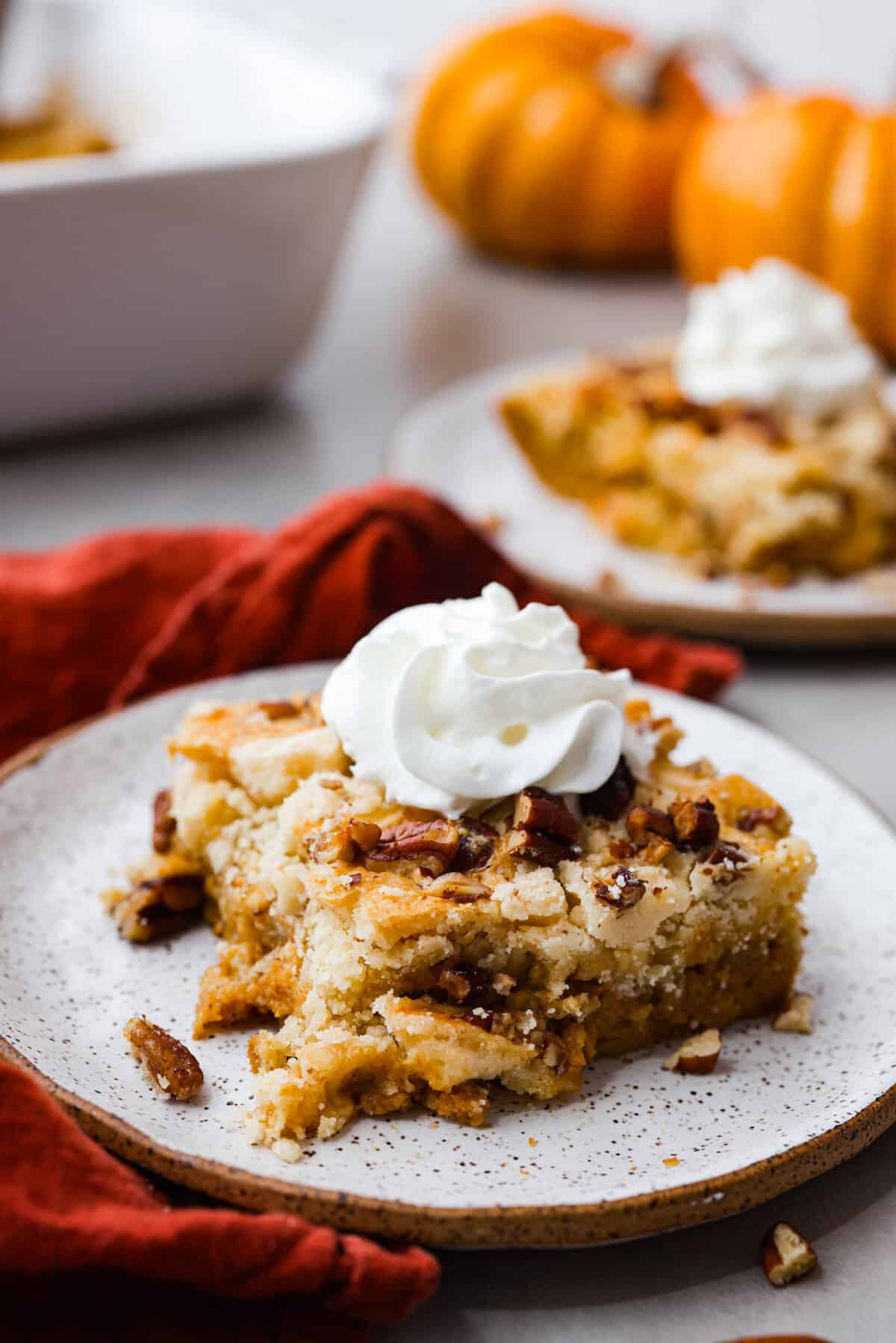 A plate with a slice of baked pumpkin dump cake with a dollop of whipped cream on top. 