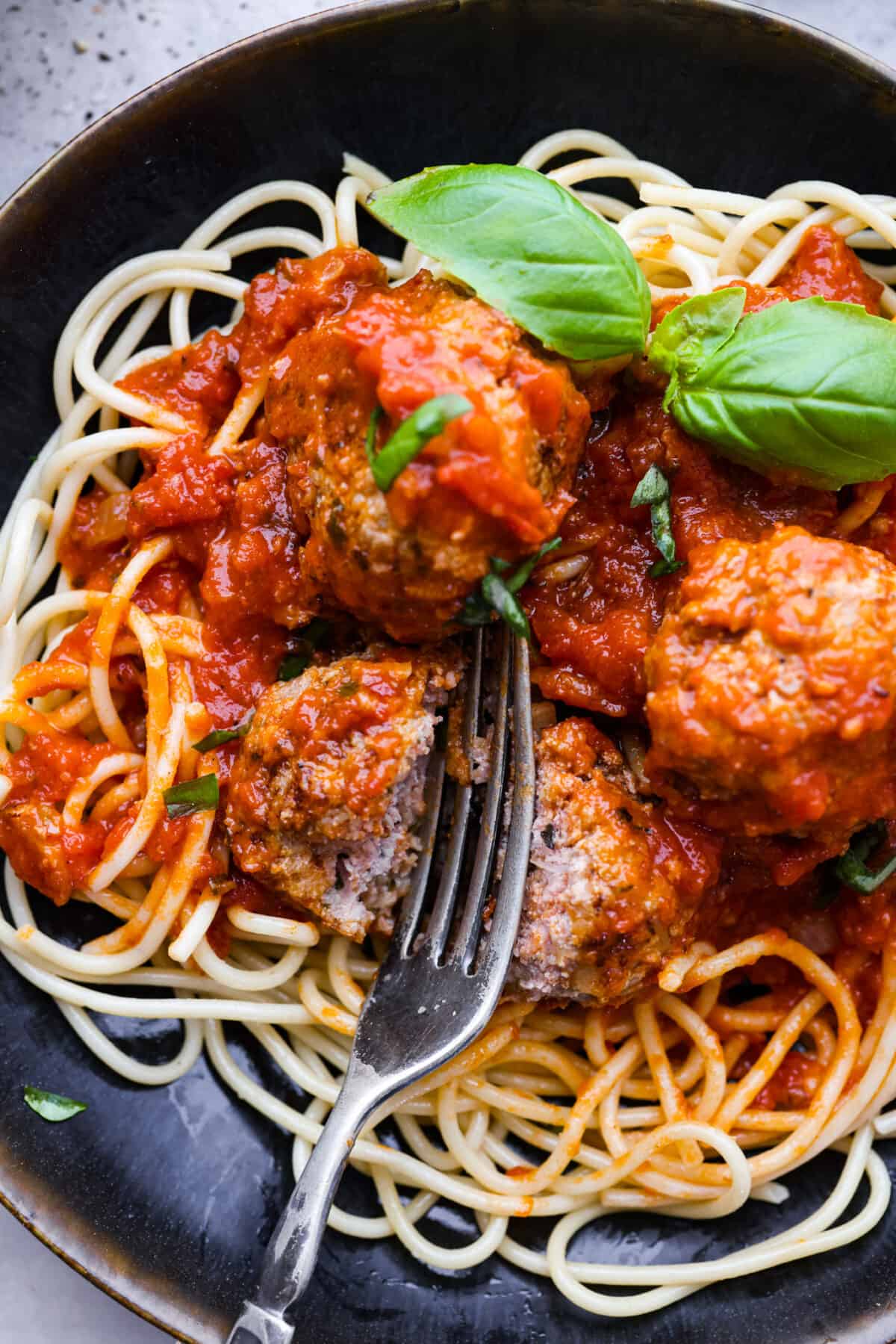 Close view of a fork cutting into a meatball with marinara and noodles.