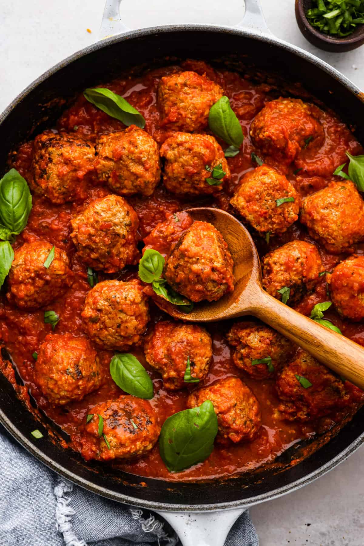 Top view of ricotta meatballs and marinara sauce in a black skillet. A wooden spoon is lifting up a meatball.