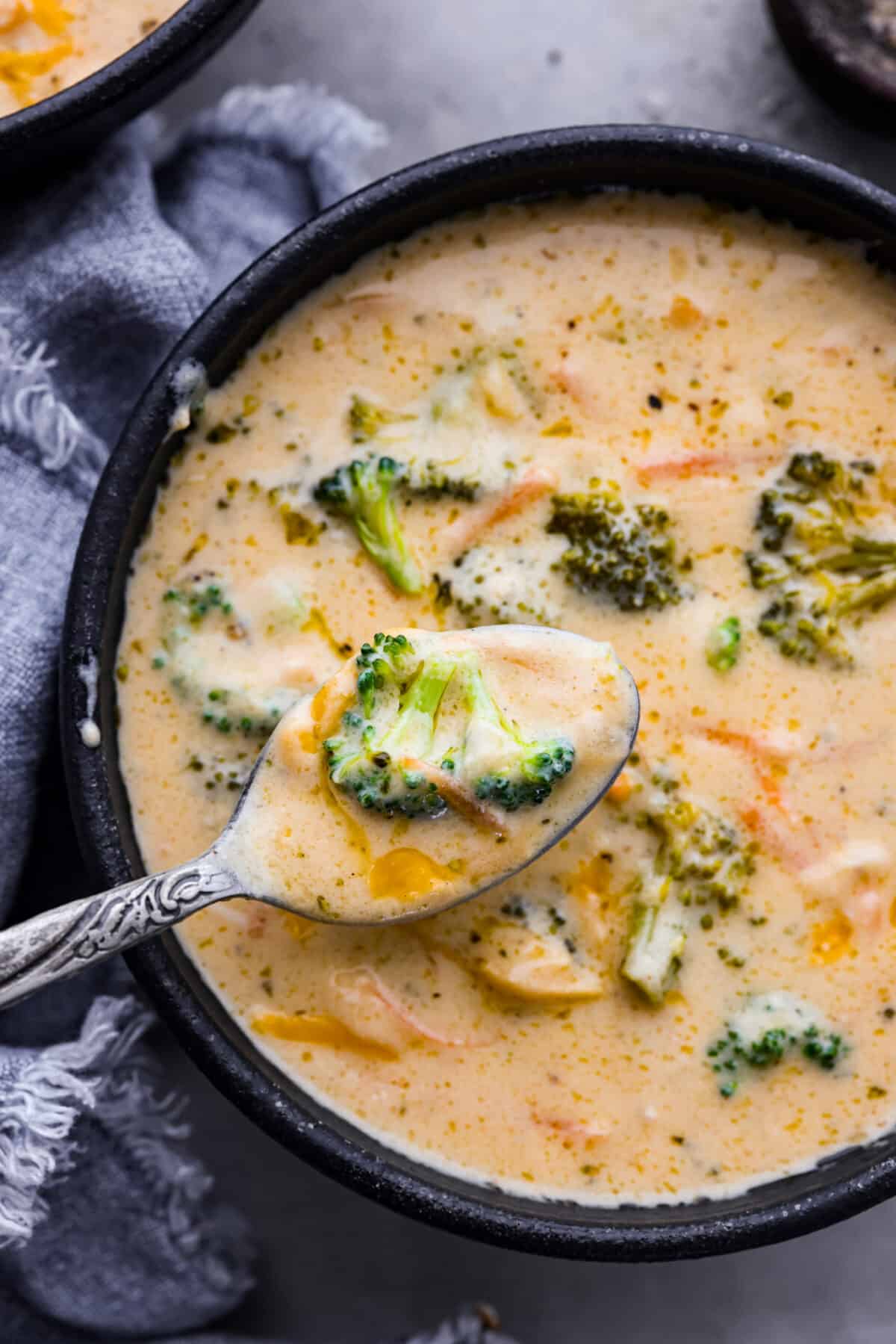 A close up of the broccoli cheese soup in a bowl with a spoon scooping some out. 