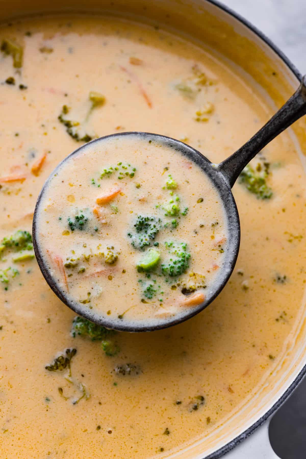 A pot of broccoli cheese soup with a ladle serving some, 