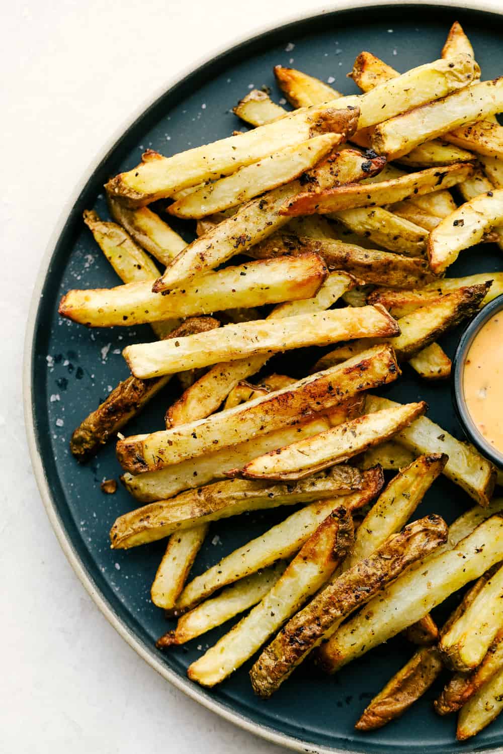 Air fryer French fries served on a black plate with a creamy dipping sauce.