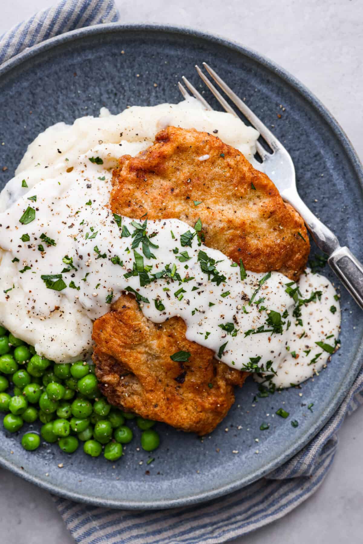 A chicken fried steak served with mashed potatoes, cream gravy, and peas.