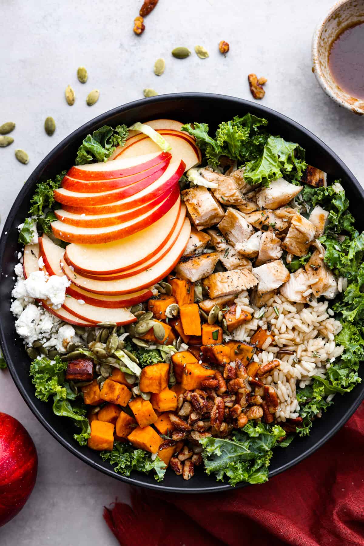 Top-down view of a salad made with kale, apples, chicken, wild rice, sweet potatoes, pecans, and goat cheese.