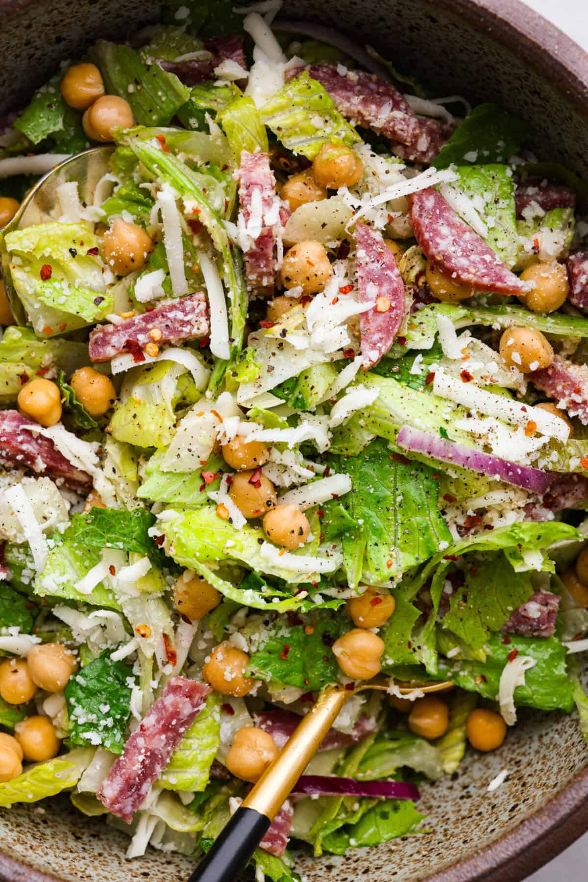 Closeup of salad made with salami, chickpeas, lettuce, and grated cheese.