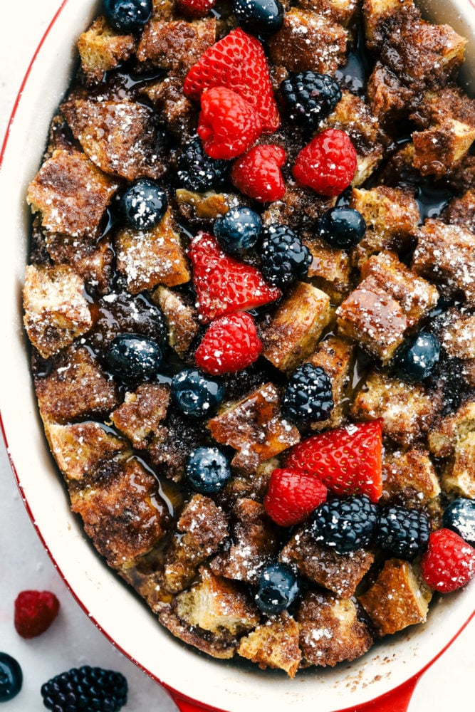 Baked French toast in a pan with fresh raspberries, strawberries and blueberries over top. 