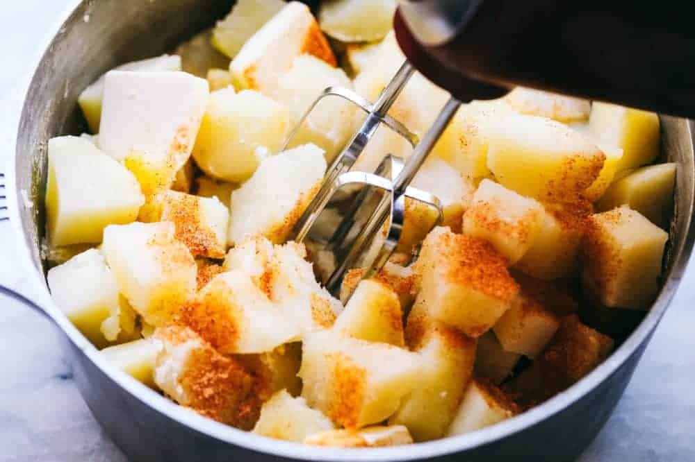 A sauce pan full of soft moist potatoes that are tender from being boiled together with seasoning. Being blended together with a hand mixer