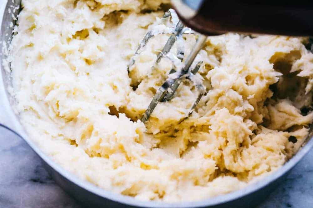 Mashed potatoes being blended together with a hand mixer in a sauce pan.