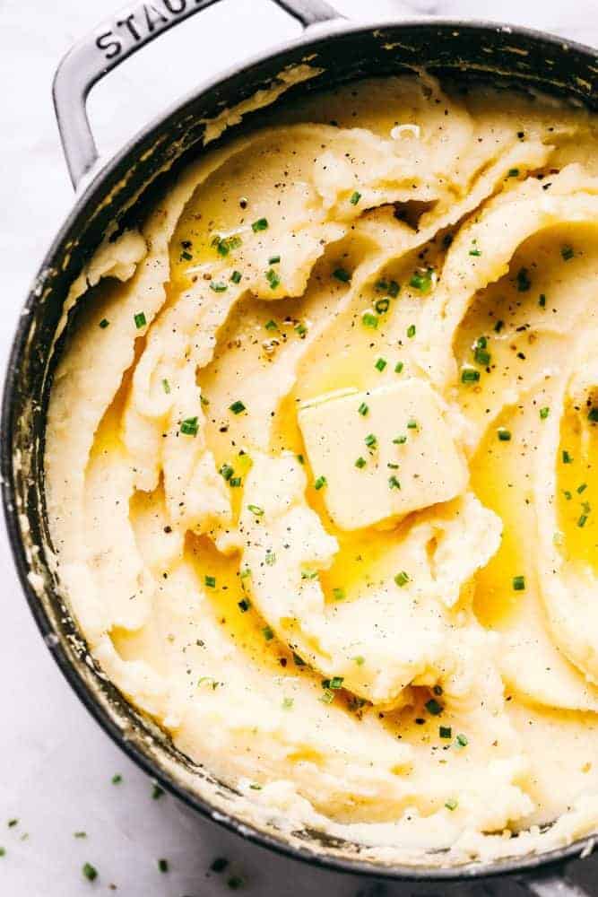 Mashed potatoes in a Staub sauce pan with a slice of butter melted on top of the mashed potatoes with chives garnished on top.