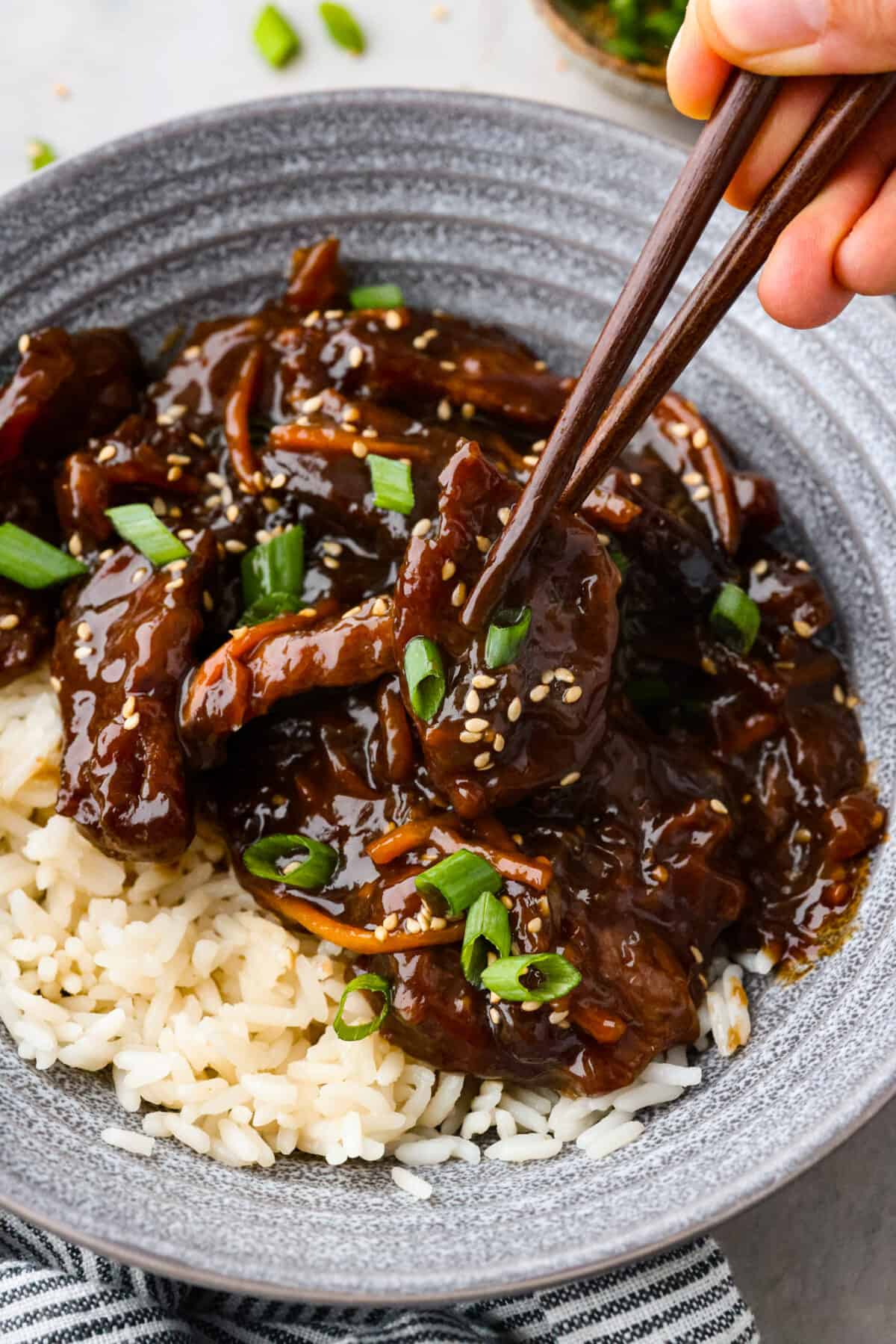 Close view of chopsticks lifting up beef from a bowl of slow cooker Mongolian beef over rice.