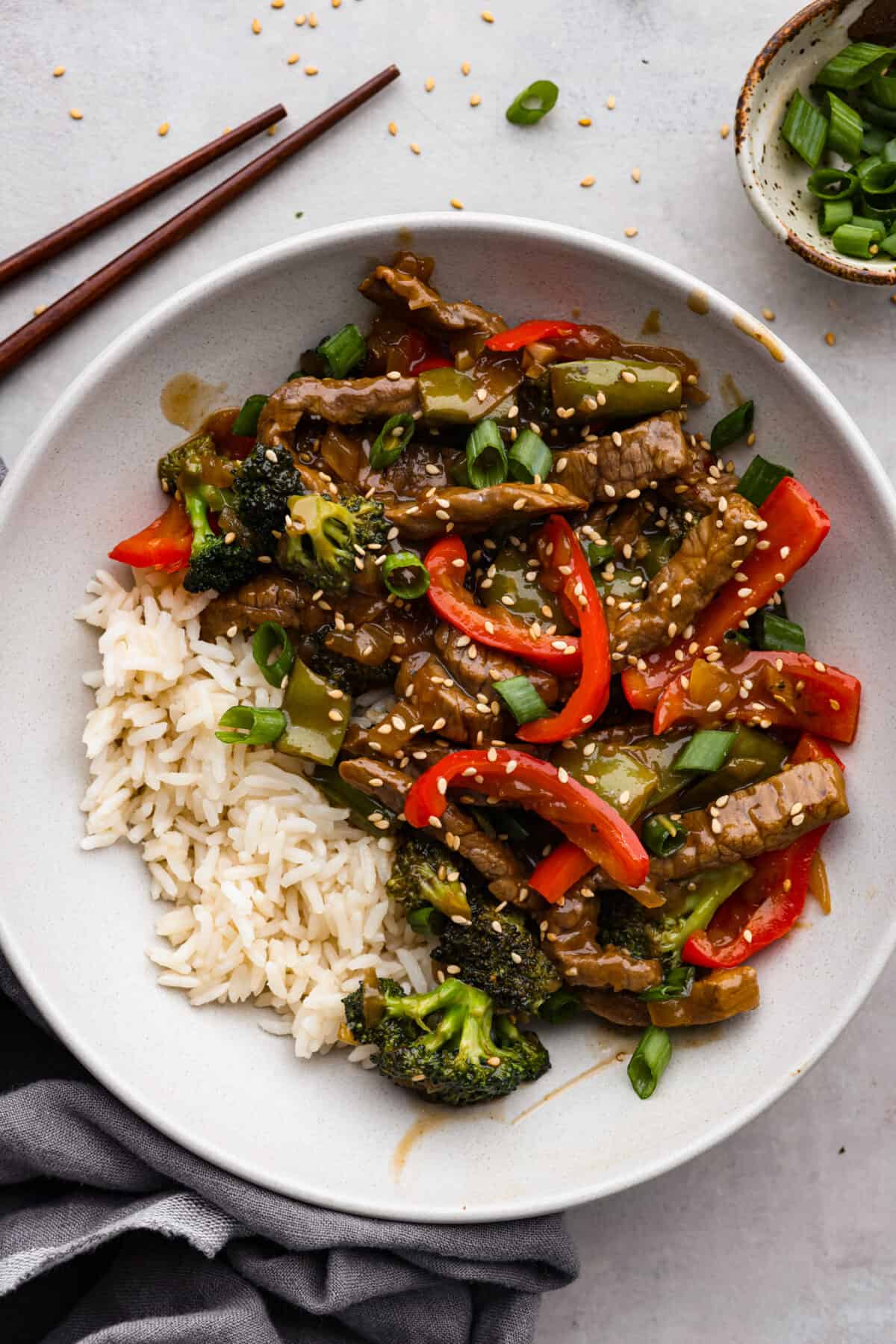 Szechuan beef and veggies served with rice in a white bowl.
