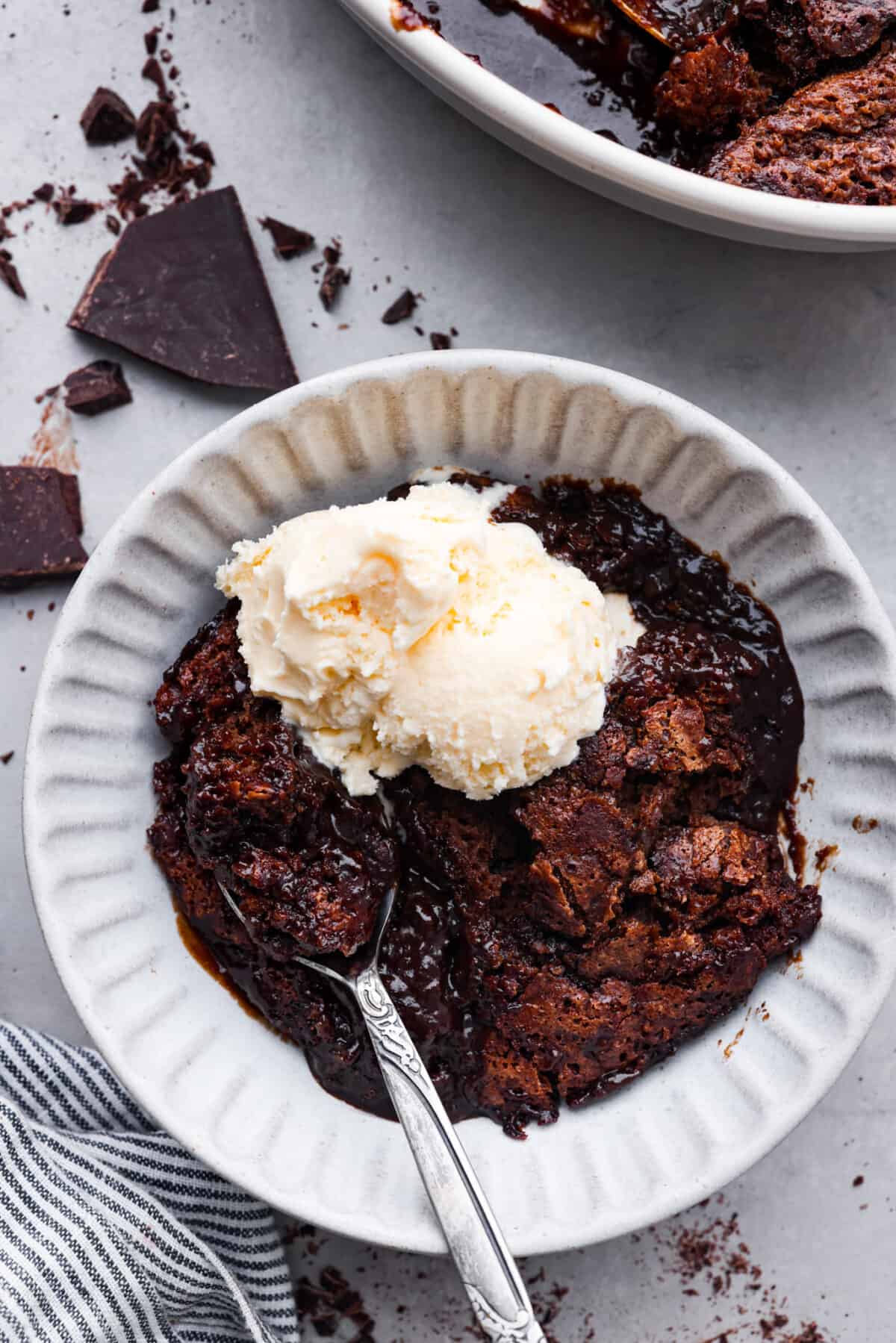 A bowl of chocolate cobbler with a silver spoon and a scoop of vanilla ice cream on top. 