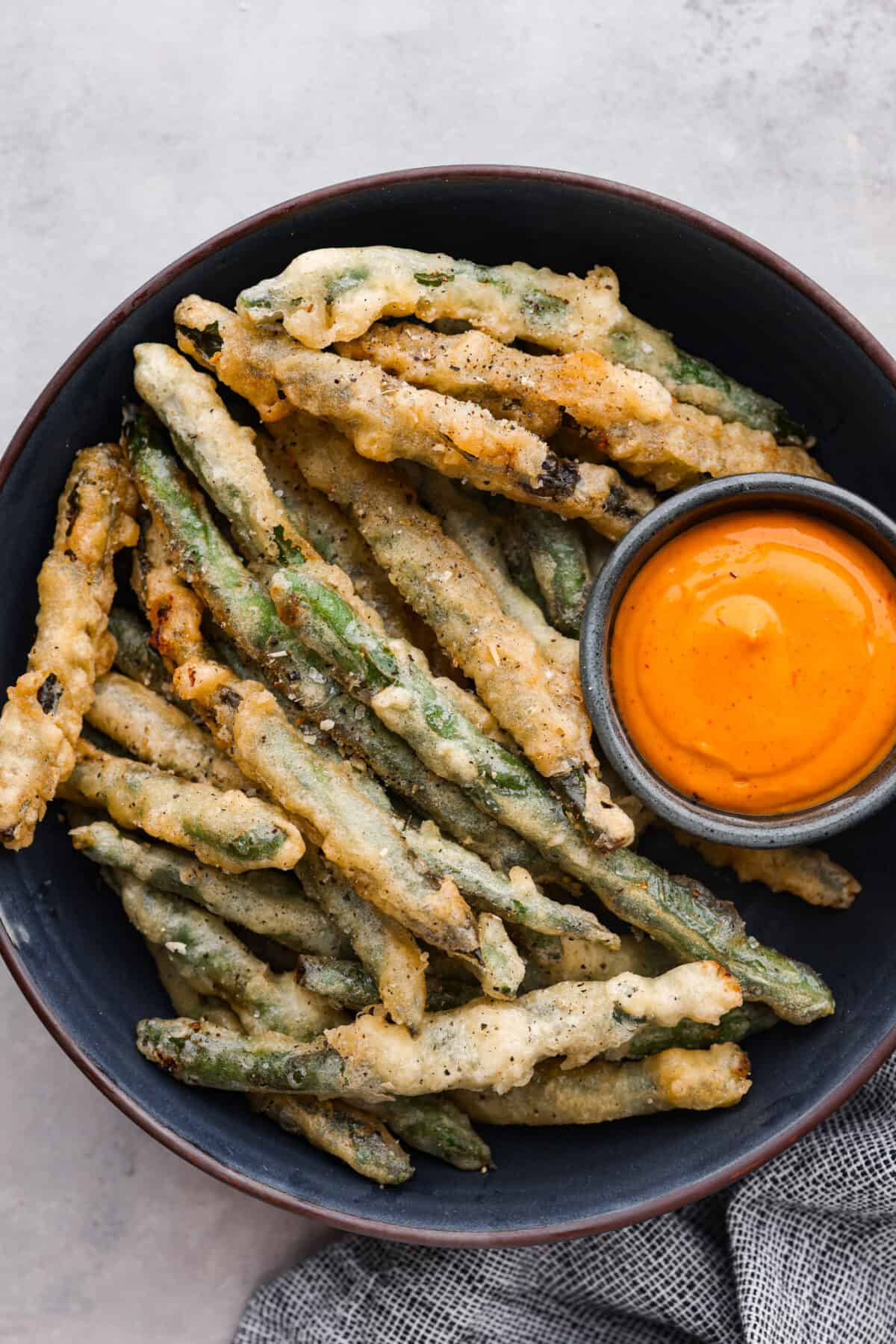 A bowl of fried green beans with a small bowl of orange dipping sauce. 