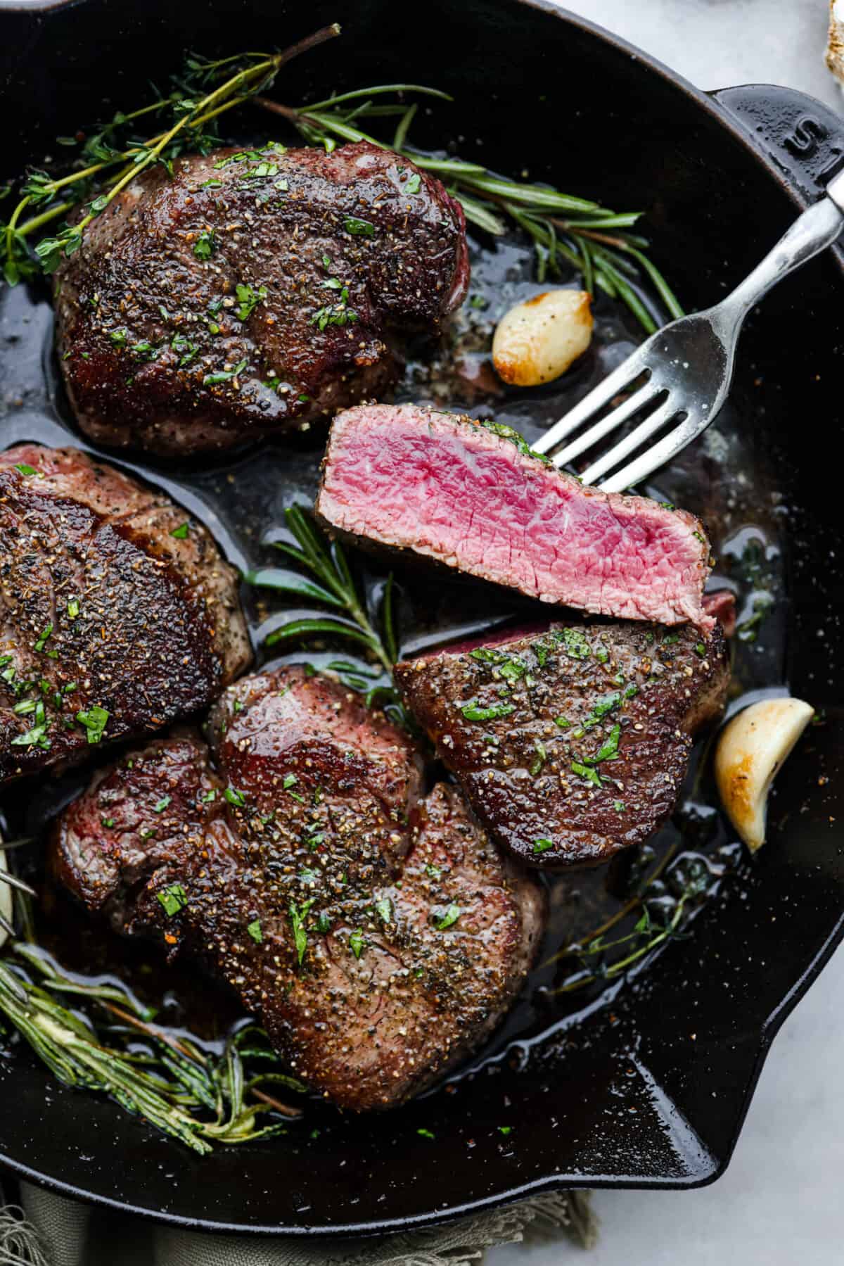 Top view of filet mignon in a black cast iron skillet with herbs and garlic.