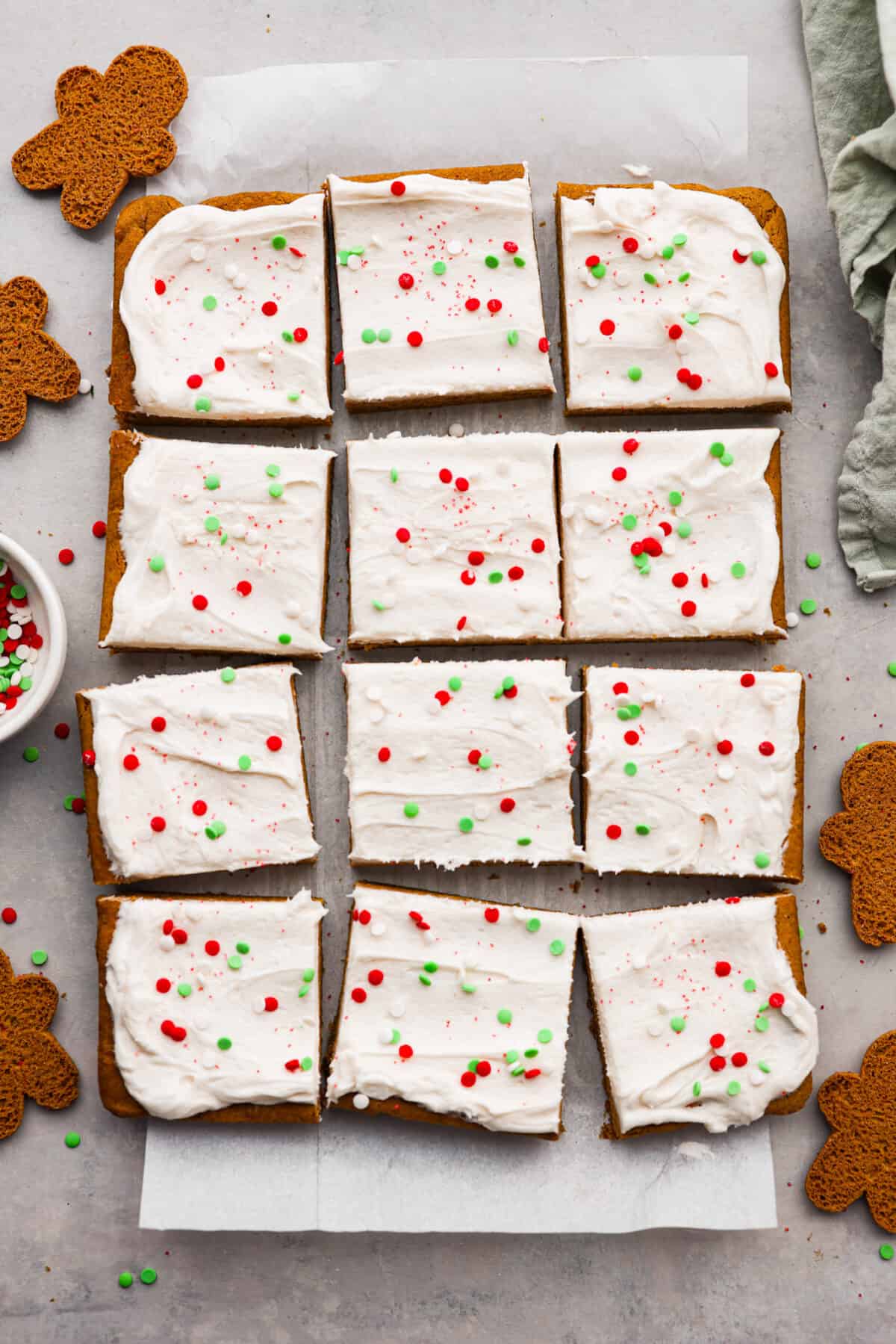 Top view of gingerbread cookie bars cut into squares on parchment paper. Sprinkles and gingerbread men are scatted around the bars. 