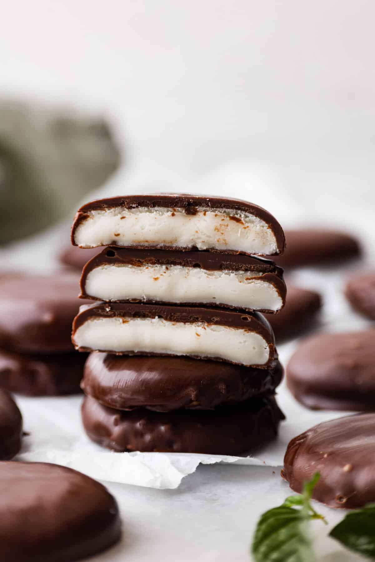 5 peppermint patties stacked on top of each other, a few of them are broken in half so the filling can be seen.